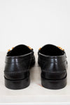 Pair of black loafers with gold accents on a white background