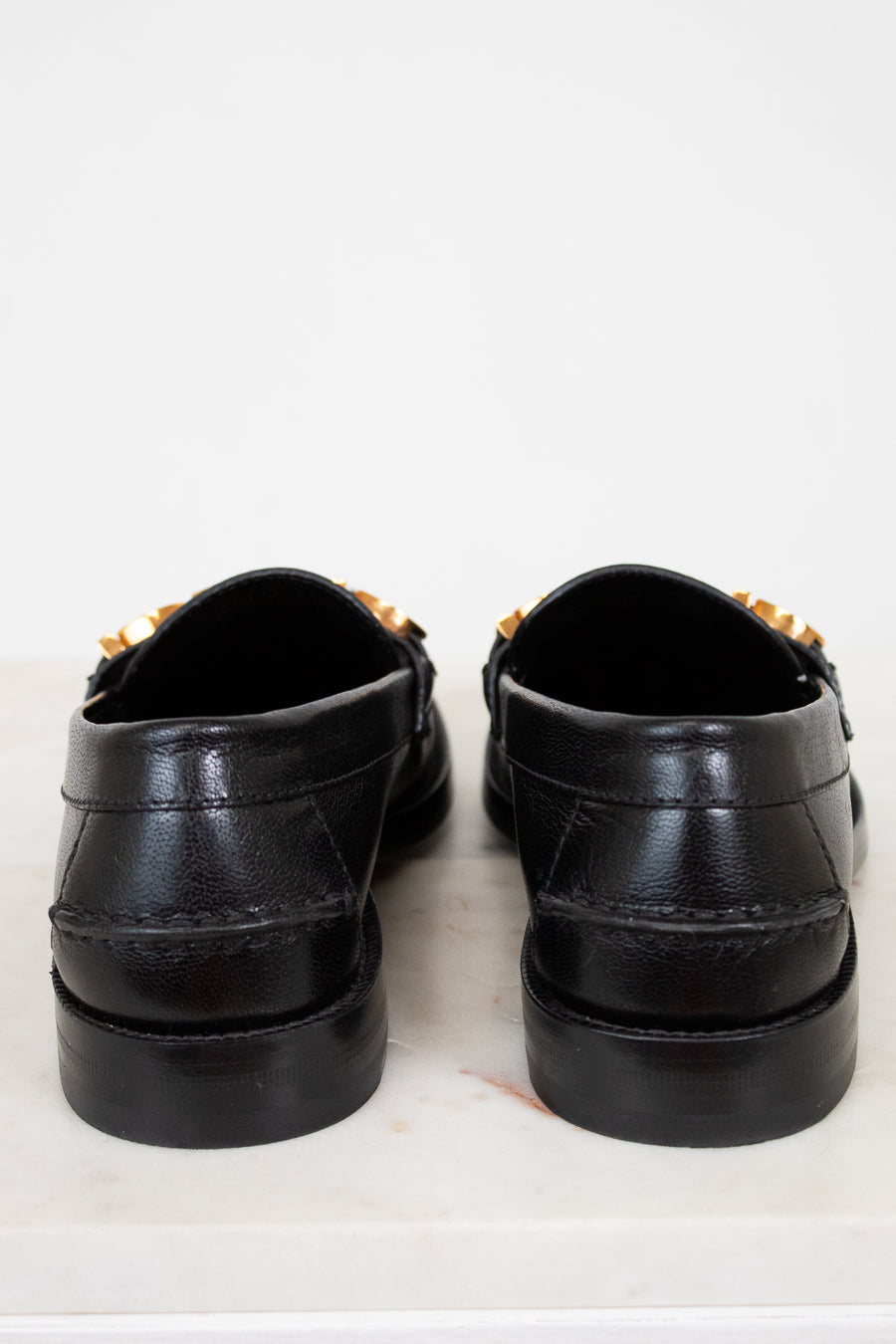 Pair of black loafers with gold accents on a white background