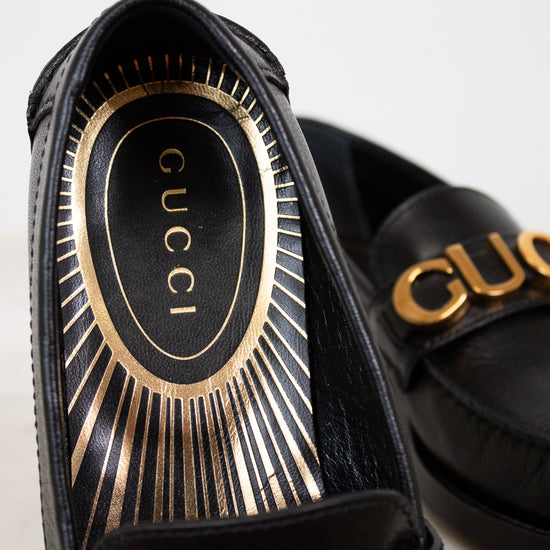 Black Gucci sandals with gold accents on a light background
