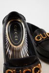 Black Gucci sandals with gold accents on a light background