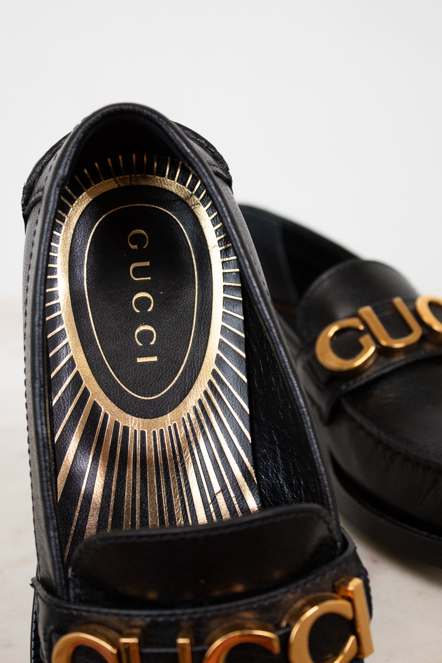 Black Gucci sandals with gold accents on a light background