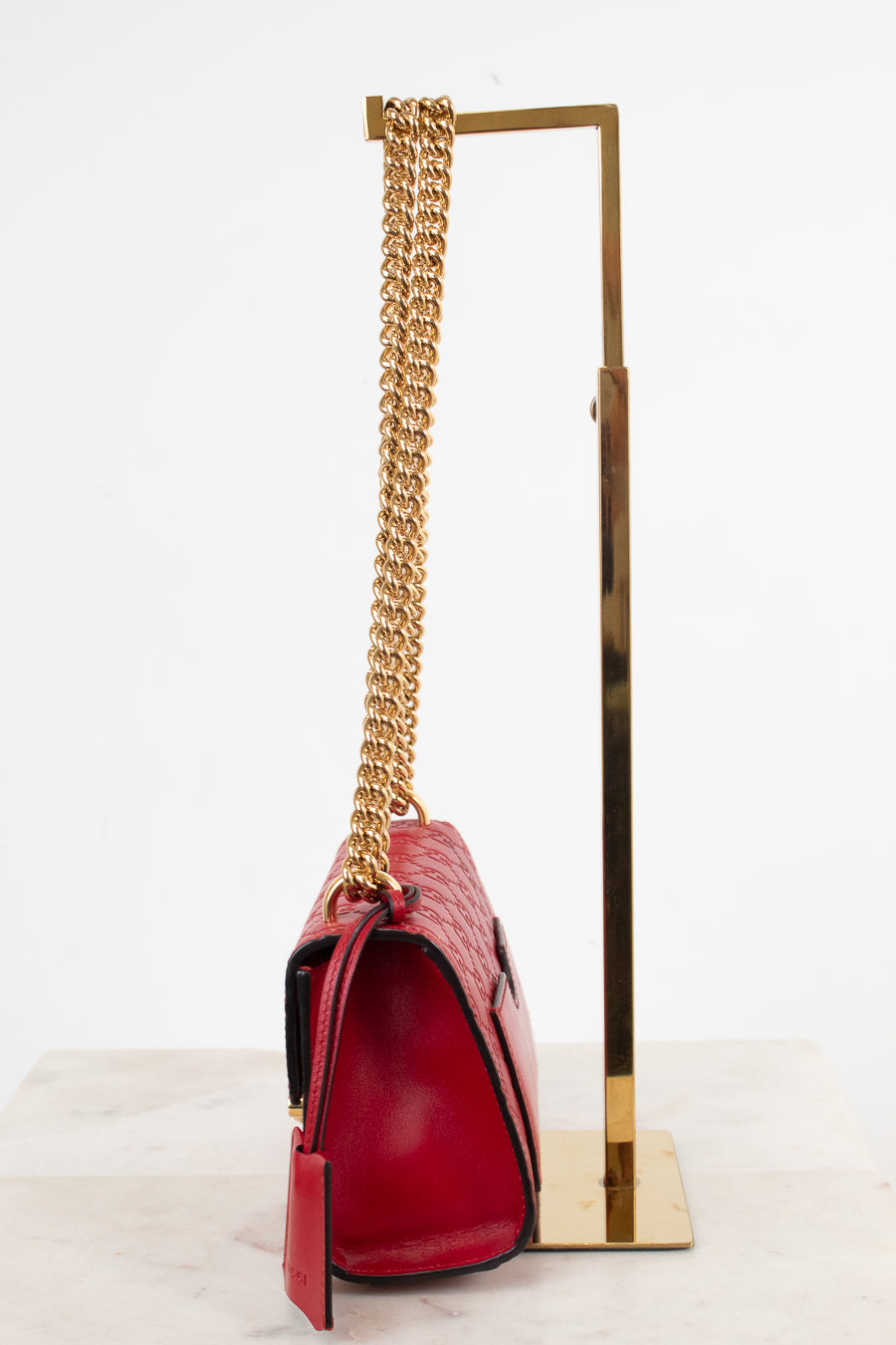 A red crocodile-embossed leather handbag with a gold chain strap, displayed on a gold metal stand against a white background.