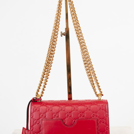 A red Gucci shoulder bag with embossed GG monogram pattern, gold chain strap, and gold-tone hardware, displayed on a stand against a white background.