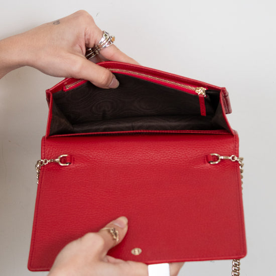Red handbag with gold chain handle held by a person against a neutral background