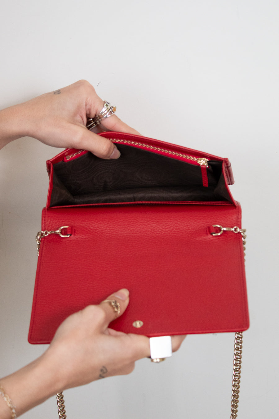 Red handbag with gold chain handle held by a person against a neutral background