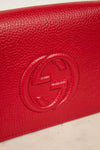 Red leather wallet with a "GG" Gucci brand logo on a light beige background