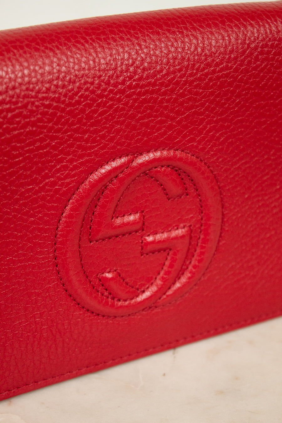 Red leather wallet with a "GG" Gucci brand logo on a light beige background