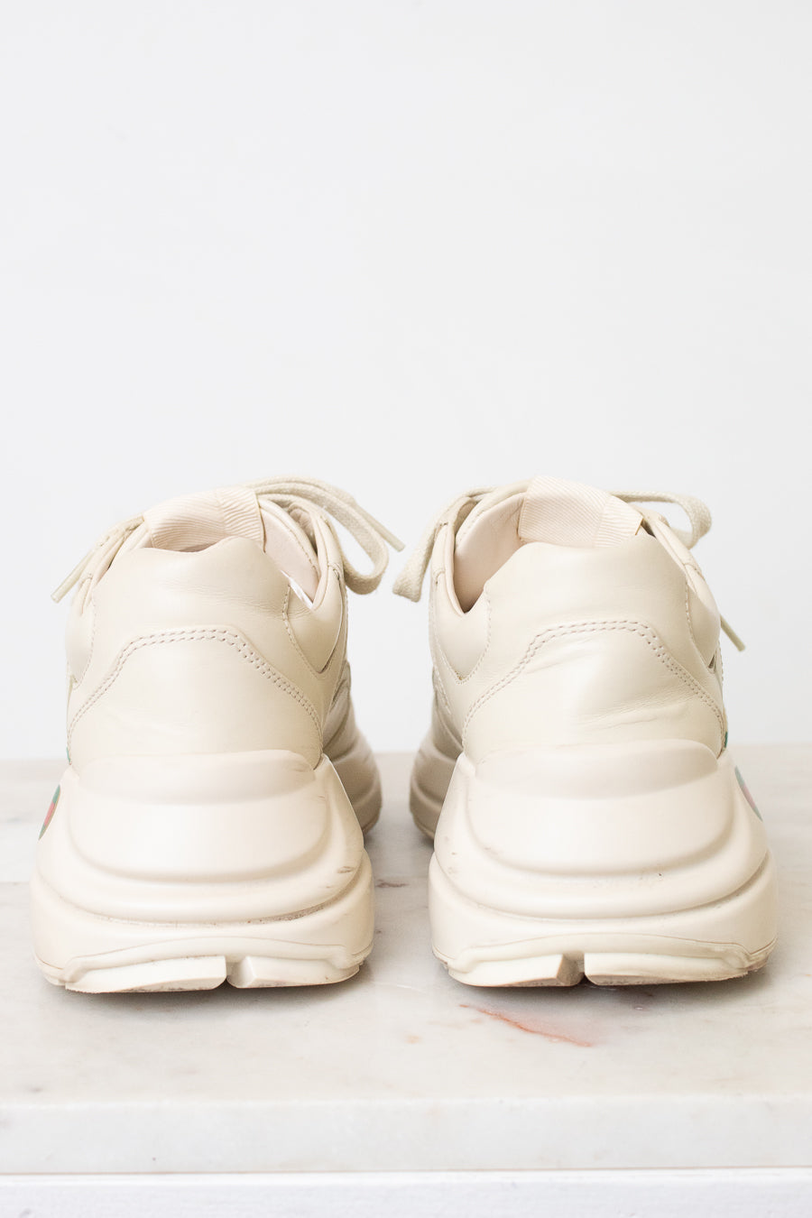 A pair of off-white Gucci sneakers shown from the back sitting on a light marble and against a light background.