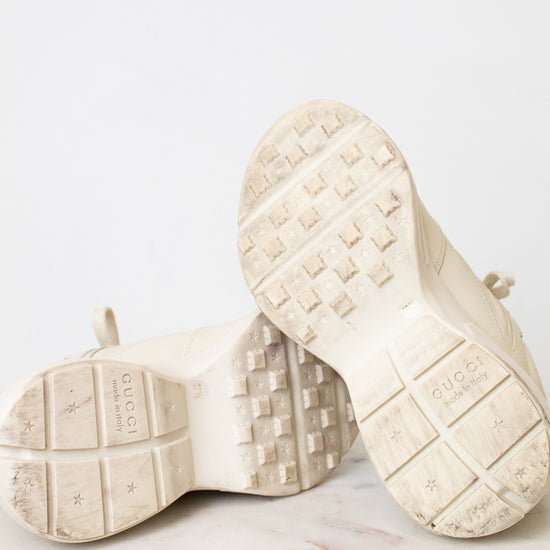 A pair of off-white Gucci chunky sneakers with white soles displayed on a light marble surface against a white background.