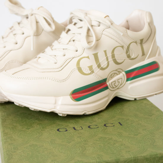 A pair of off-white Gucci sneakers displayed on top of a green Gucci shoebox against a light background.