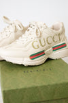 A pair of off-white Gucci sneakers displayed on top of a green Gucci shoebox against a light background.