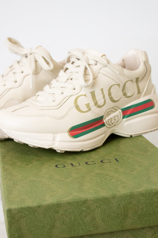 A pair of off-white Gucci sneakers displayed on top of a green Gucci shoebox against a light background.