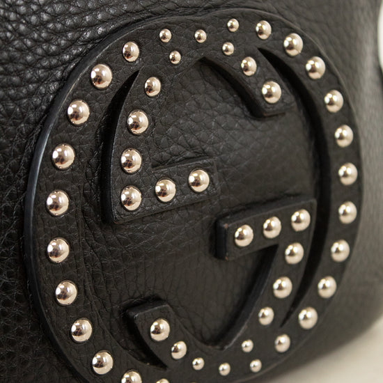 Close-up of a black pebbled leather Gucci bag featuring the brand's interlocking GG logo adorned with silver-tone studs.