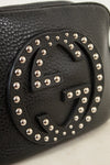 Close-up of a black pebbled leather Gucci bag featuring the brand's interlocking GG logo adorned with silver-tone studs.