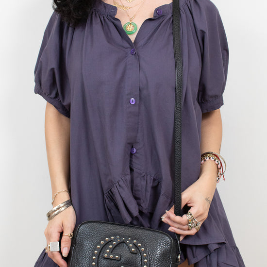 A woman wearing a dark purple puff-sleeve blouse and holding a black Gucci shoulder bag with the brand's interlocking GG logo.
