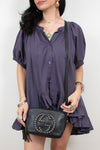 A woman wearing a dark purple puff-sleeve blouse and holding a black Gucci shoulder bag with the brand's interlocking GG logo.