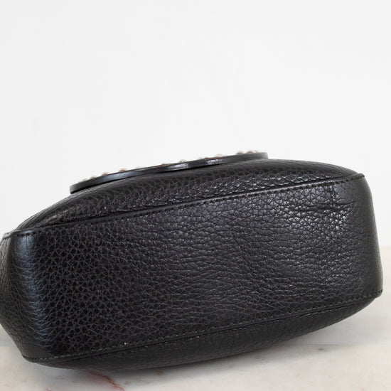 A close-up of a black pebbled leather clutch or small handbag resting on a light marble surface against a white background.