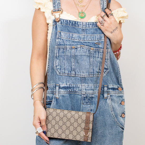 Person wearing denim overalls holding a Gucci handbag against a plain background