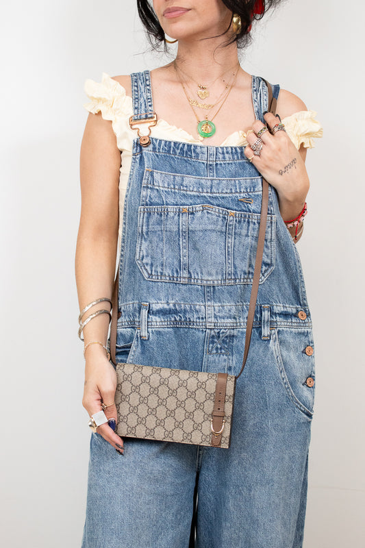 Person wearing denim overalls holding a Gucci handbag against a plain background