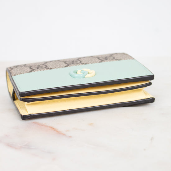 A Gucci wallet in beige GG Supreme canvas, featuring a interlocking G logo on the front, resting on a white marble surface.