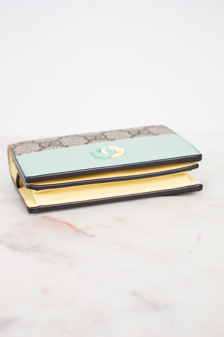 A Gucci wallet in beige GG Supreme canvas, featuring a interlocking G logo on the front, resting on a white marble surface.