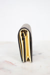 A close-up side view of a slim bifold wallet standing upright on a light marble surface against a white background. The wallet has a textured beige monogram exterior with a bright yellow interior lining.