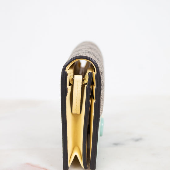 A close-up side view of a wallet standing upright on a light marble surface against a white background, showing a textured exterior, black piping trim, and prominent pale yellow interior.
