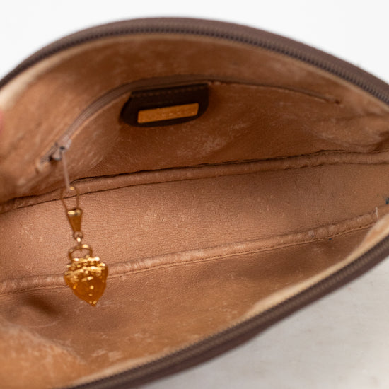 Close-up of the interior of a brown zippered pouch or clutch, showing a tan satin lining, a small interior label, and a dangling gold zipper pull.