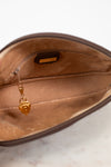 Close-up of the interior of a brown zippered pouch or clutch, showing a tan satin lining, a small interior label, and a dangling gold zipper pull.