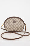 A vintage Gucci oval shoulder bag in the classic GG Supreme canvas, featuring a brown leather trim and strap, resting on a white marble surface against a white background.
