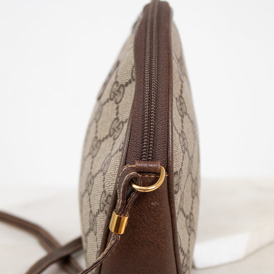 A vintage Gucci monogram canvas pouch with brown leather trim and gold-tone hardware, shown from a side profile view on a light marble surface.