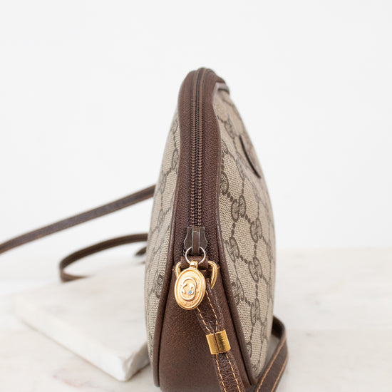 A Gucci shoulder bag in beige GG Supreme canvas with brown leather trim and gold-tone hardware, shown from a side profile on a light marble surface against a white background.