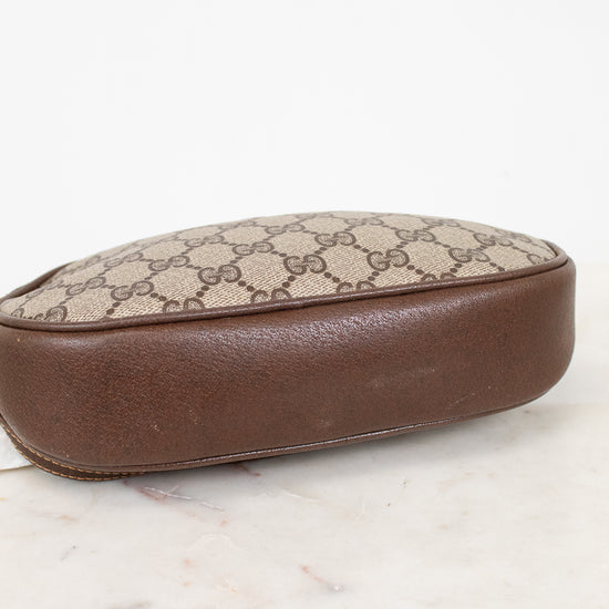 A vintage Gucci pouch featuring the classic GG Supreme canvas in beige and brown, finished with a smooth brown leather base, shown on a white marble surface against a white background.