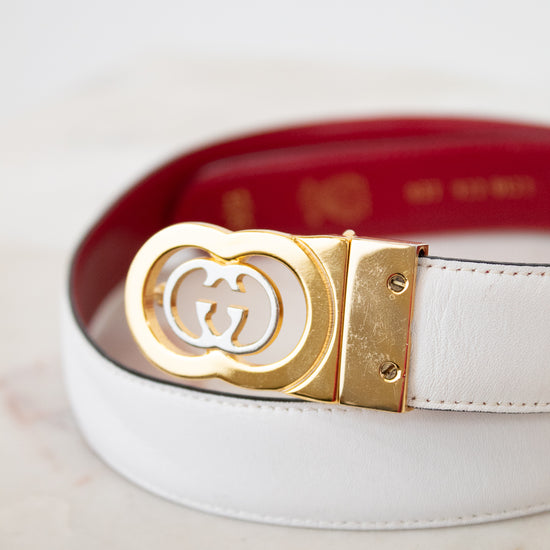 White and red reversible belt with a gold and silver Gucci buckle on a light background