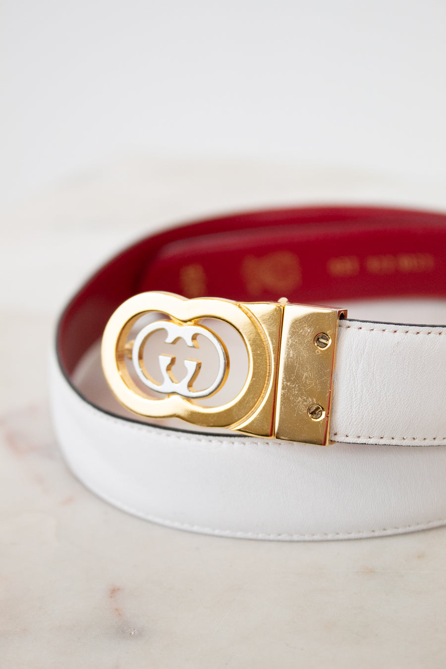 White and red reversible belt with a gold and silver Gucci buckle on a light background