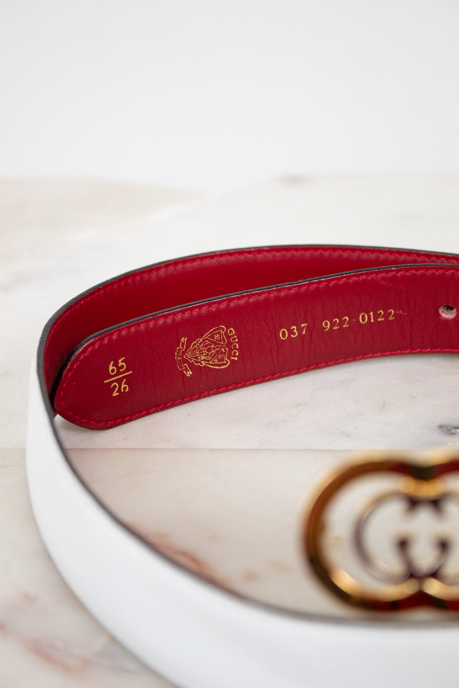 White and red belt with gold and silver logo and gold text interior on a marble surface