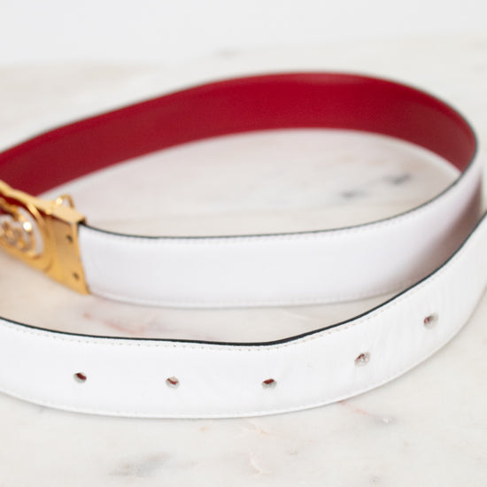 White and red reversible belt with a gold and silver buckle on a marble surface