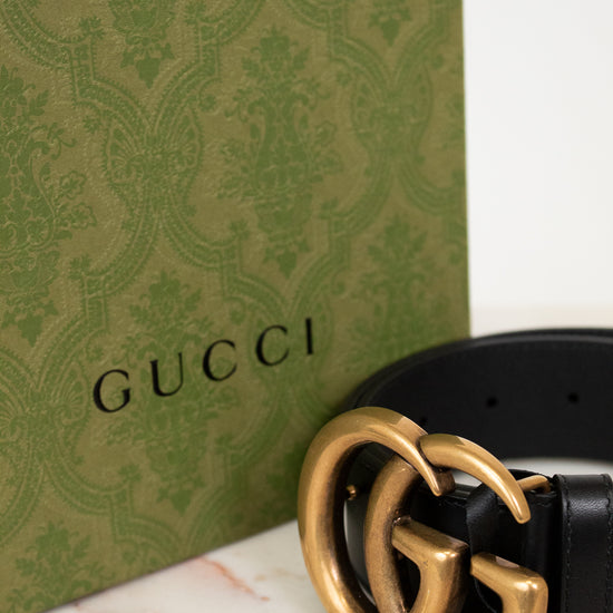 Gucci belt with gold buckle on a marble surface next to a Gucci box.
