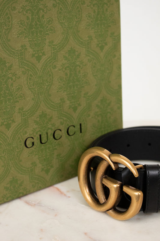 Gucci belt with gold buckle on a marble surface next to a Gucci box.