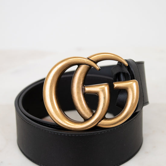 Black belt with gold double G buckle on a light marble background