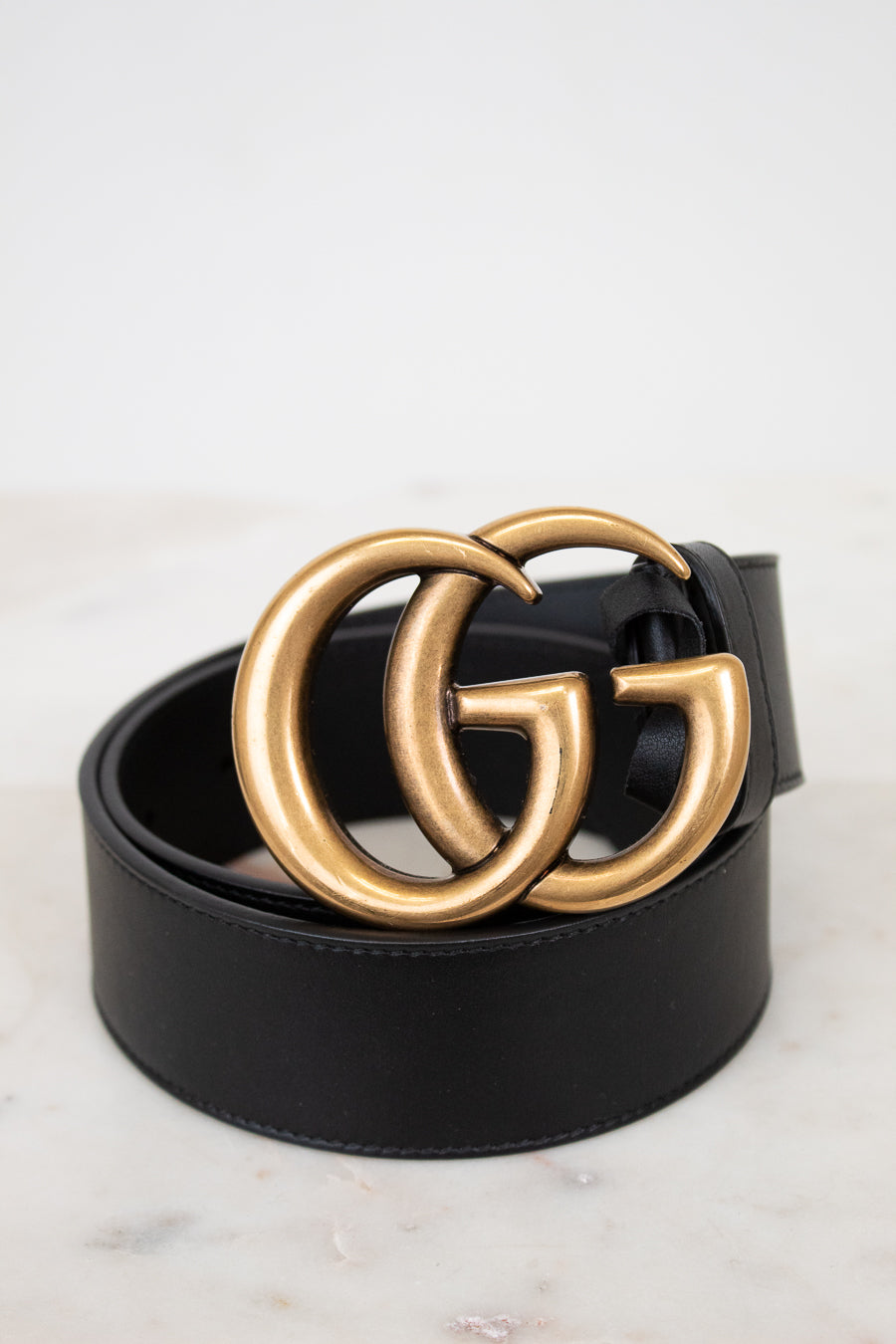 Black belt with gold double G buckle on a light marble background