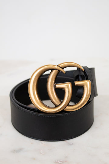 Black belt with gold double G buckle on a light marble background