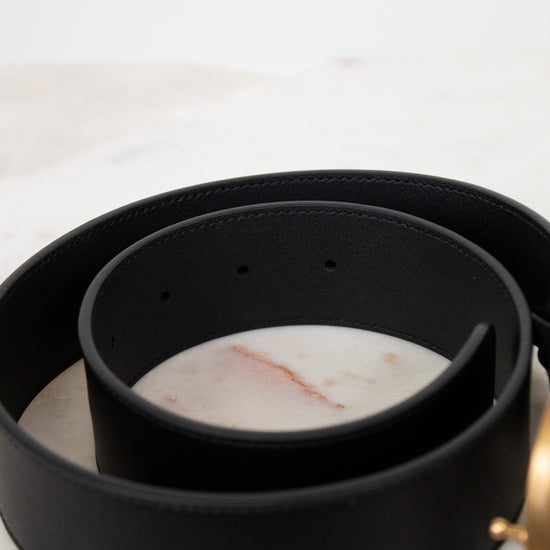 Black leather belt with a gold buckle on a marble surface