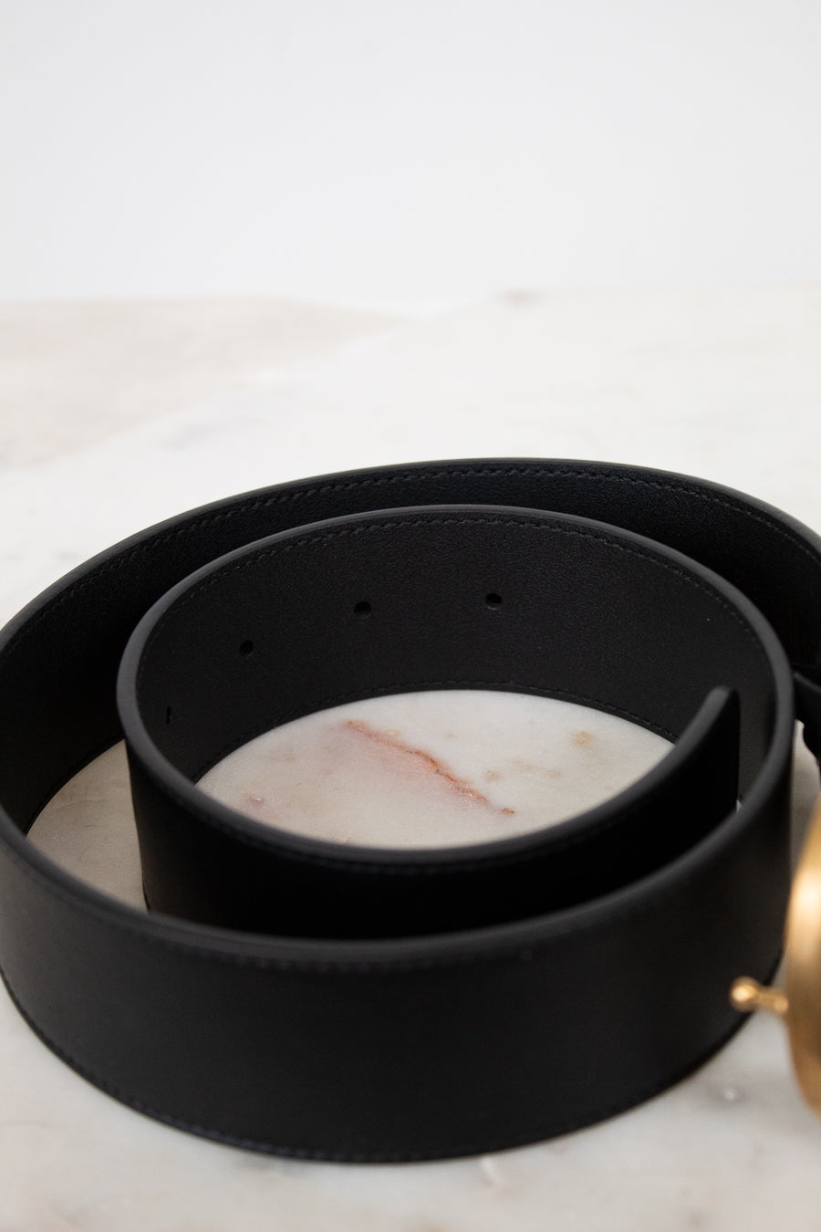 Black leather belt with a gold buckle on a marble surface