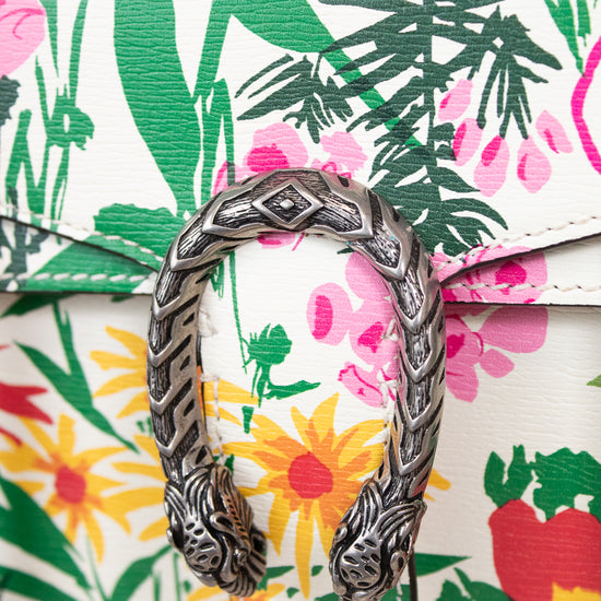 A close-up of a Gucci flap bag featuring a vibrant tropical floral print with green palm leaves, pink flowers, and yellow sunflowers on a white base, accented by a prominent silver-tone dionysus closure.