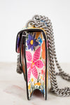 A close-up of a handbag with a colorful floral pattern and a chunky silver chain strap, set against a clean white background.