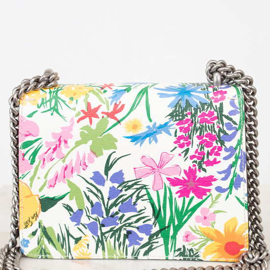 A rectangular shoulder bag with a vibrant multicolor floral print on a white background, featuring a silver-tone metal chain strap, photographed on a light marble surface against a white background.