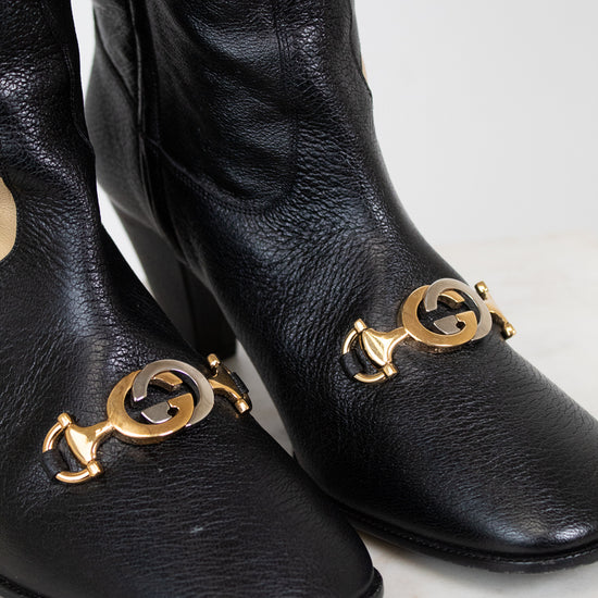 Close-up of black leather boots showing two tone 'GG' hardware along toe and set against a white background