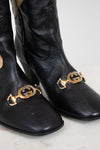 Close-up of black leather boots showing two tone 'GG' hardware along toe and set against a white background