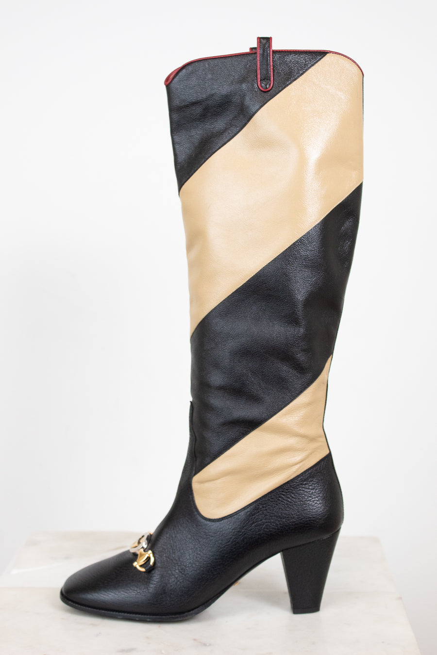 Side profile of black and beige asymmetrical leather stripes of boot with two-tone 'GG' toe detail standing against a white background